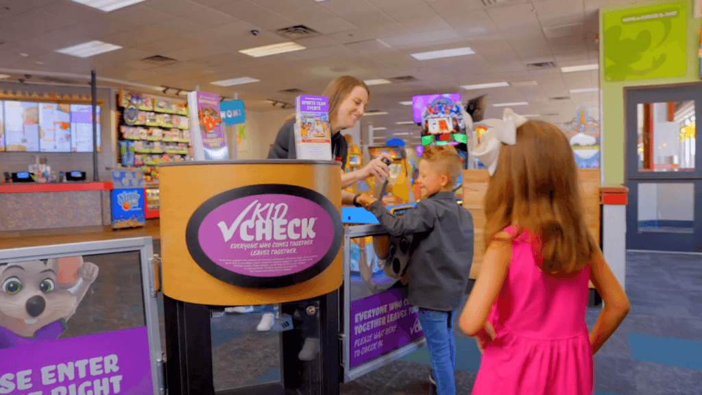 A staff member stamps a boy's hand at Chuck E. Cheese Kid Check as kids line up for arcade games during a birthday party.