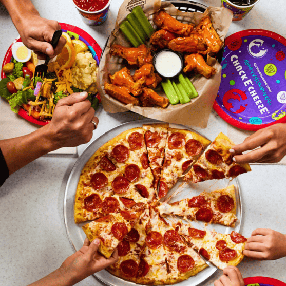 Kids share pepperoni pizza, wings, and salad at a Chuck E. Cheese birthday party table with plates, drinks, and Fun Passes nearby.