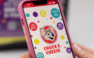 Person holding phone displaying Chuck E. Cheese website.
