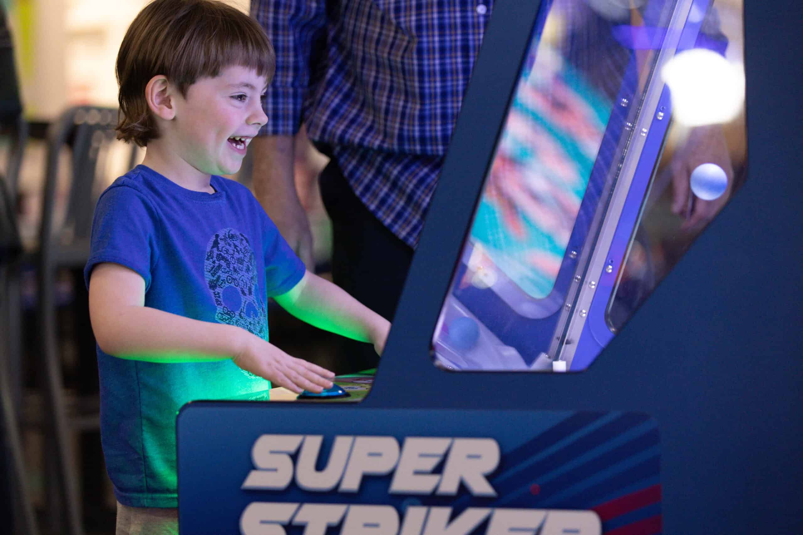 A young boy smiles while playing Super Striker arcade at Chuck E. Cheese during a kids birthday party with pizza and Fun Pass.
