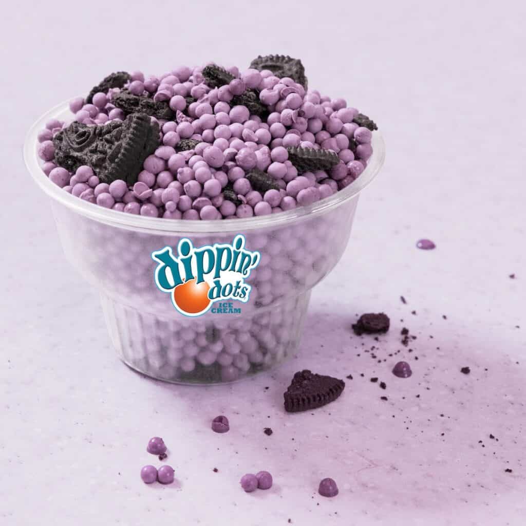 Clear cup of purple Dippin’ Dots and Oreo pieces on a purple table at Chuck E. Cheese, with scattered cookie bits nearby.