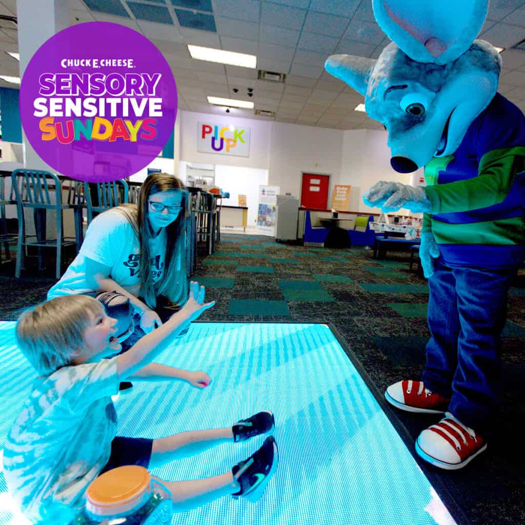 Child on glowing floor reaching for Chuck E. Cheese mascot at family fun center, Sensory Sensitive Sundays text displayed nearby.