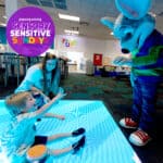 Child on glowing floor reaching for Chuck E. Cheese mascot at family fun center, Sensory Sensitive Sundays text displayed nearby.
