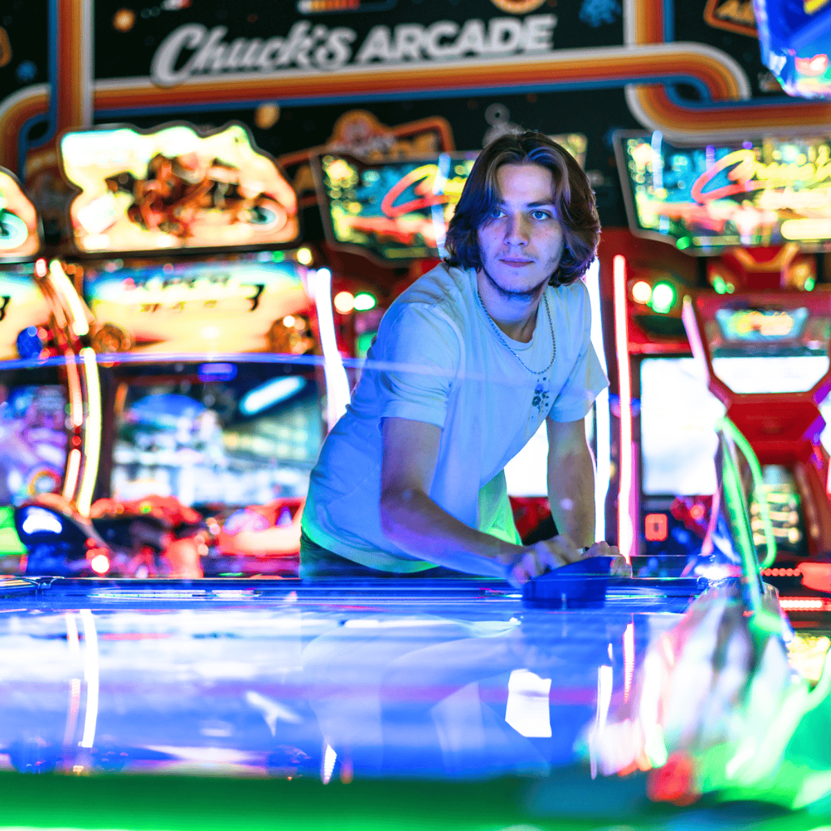 A young man plays air hockey at Chuck E. Cheese, surrounded by arcade games for kids, ideal for birthday party and family fun center events.
