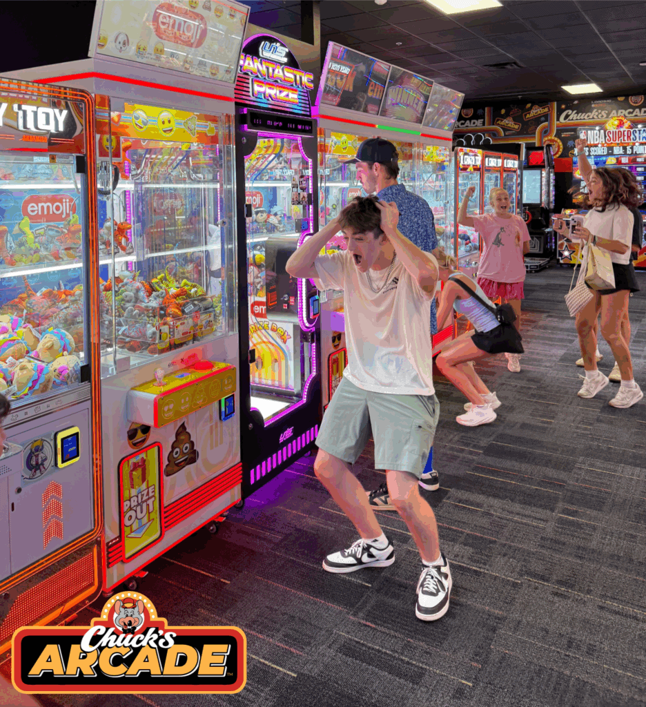 Teen boy at Chuck E. Cheese family fun center, frustrated at claw machine; kids play arcade games nearby, Chuck’s Arcade logo visible.