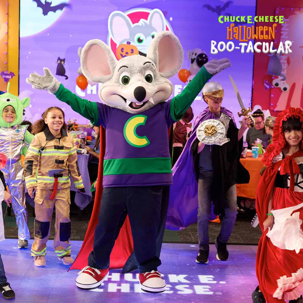 Chuck E. Cheese in a Halloween costume with kids at a birthday party, Boo-tacular banner, arcade games, pizza and Fun Pass visible.