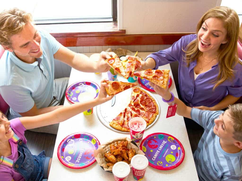 Family eating pizza at Chuck E. Cheese, viewed from overhead with the pizza as the focal point of a warm dining moment.