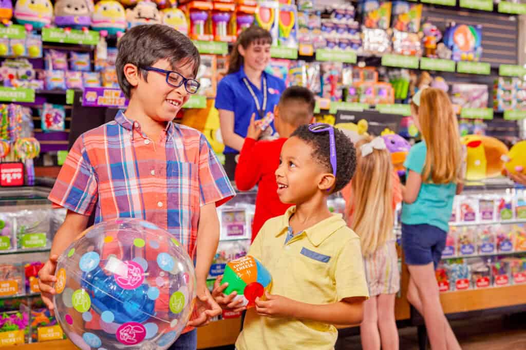 Prize counter at Chuck E. Cheese with two happy boys (ages 6–8), one holding a prize, joyful.
