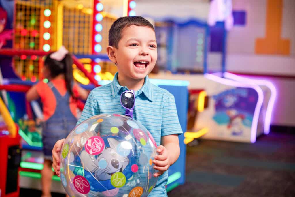 Boy age 5–7 holds a colorful cartoon ball in Chuck&nbsp;E.&nbsp;Cheese arcade games area