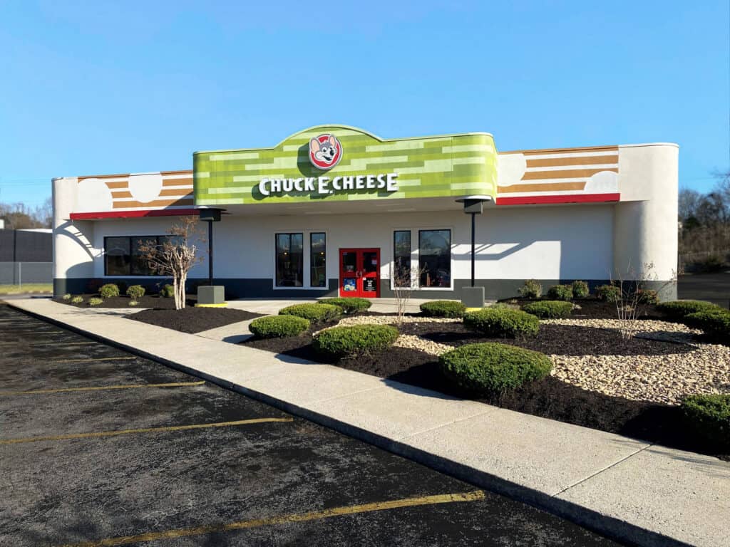 Chuck E. Cheese family fun center with green-orange sign, red double doors; exterior view.