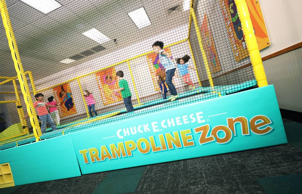 Kids jump on a trampoline at Chuck&nbsp;E.&nbsp;Cheese family fun center, near arcade games, murals, and colorful decor