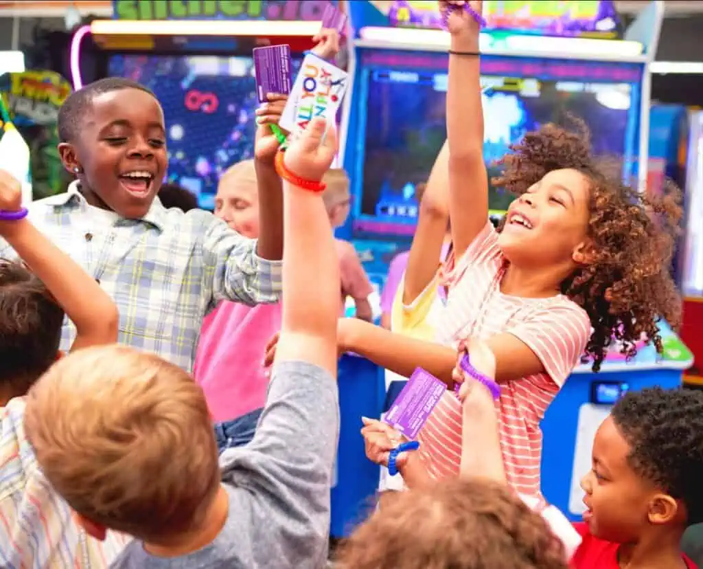 Kids at Chuck E. Cheese birthday party celebrate with tickets and prizes, surrounded by arcade games and pizza, using their Fun Pass.
