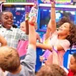 Kids at Chuck E. Cheese birthday party celebrate with tickets and prizes, surrounded by arcade games and pizza, using their Fun Pass.