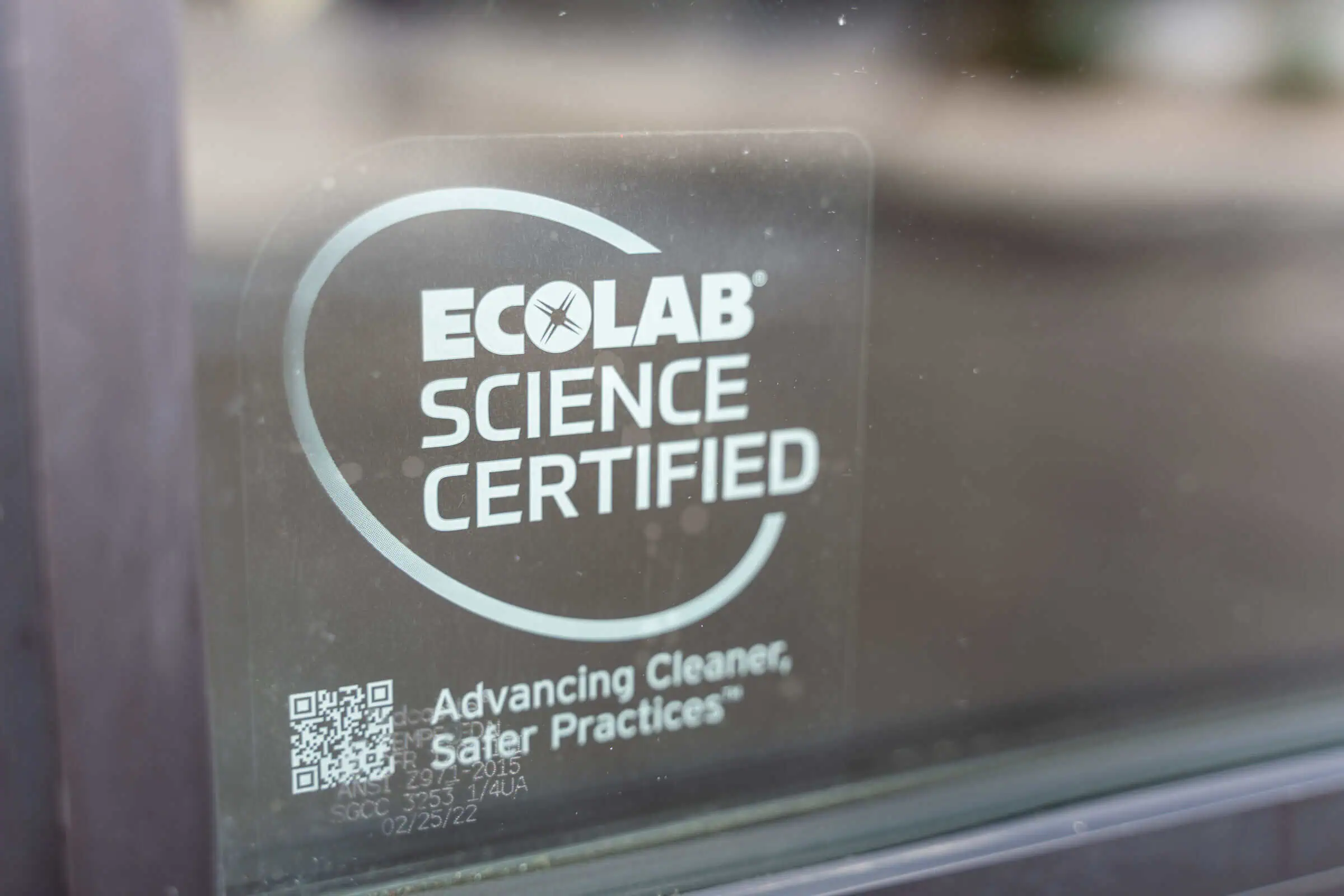 ECOLAB SCIENCE CERTIFIED sticker with safety tagline and QR code on Chuck E. Cheese glass, seen from outside the family fun center.