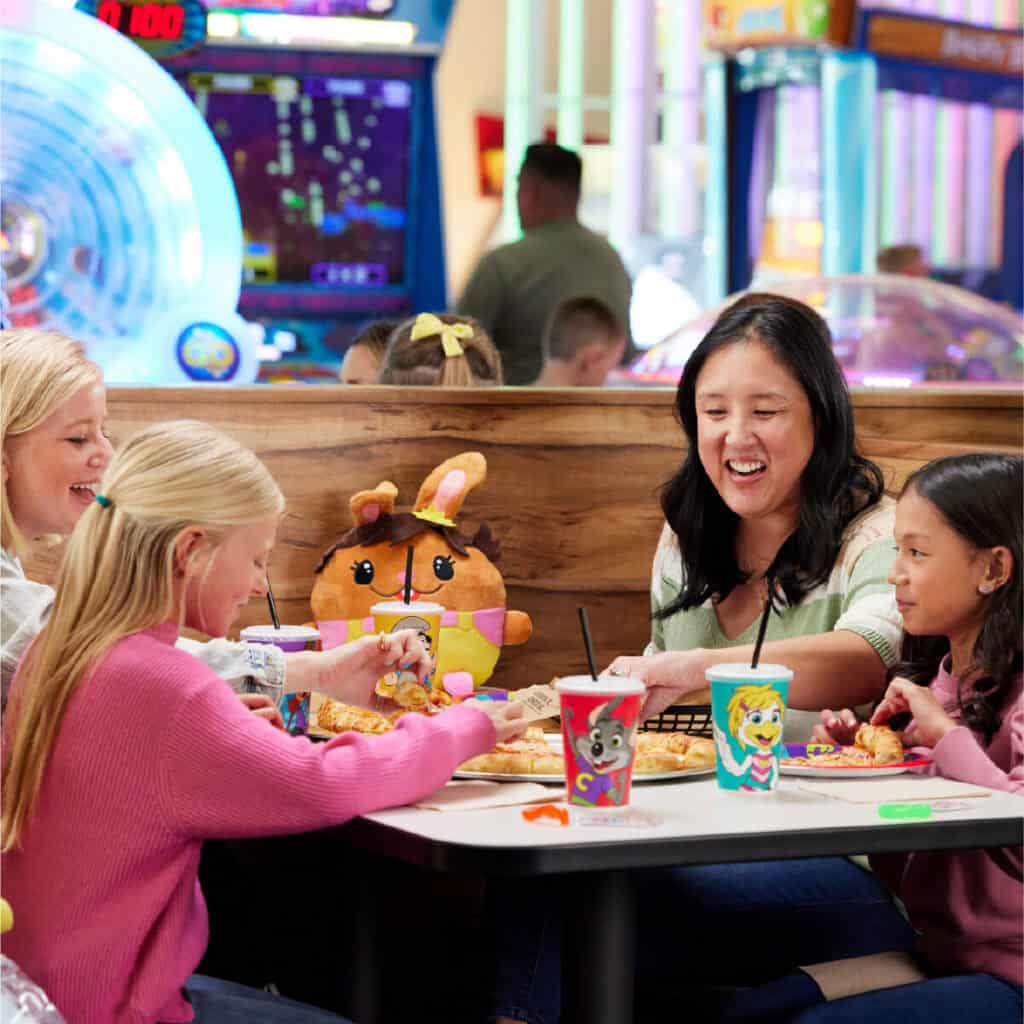 Arcade games and pizza at Chuck E. Cheese; two kids and two adults enjoy a meal in the family fun center.