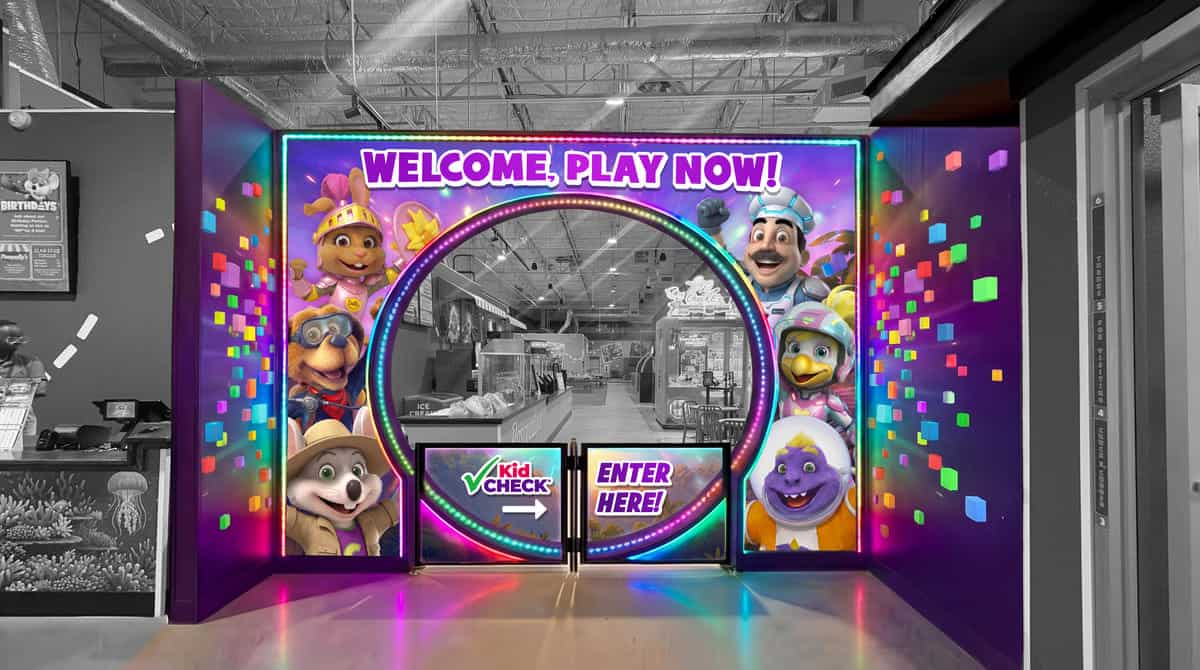 Chuck E. Cheese Play Now! entrance with mascots, circular opening to arcade games for kids; black-and-white background contrasts colors.