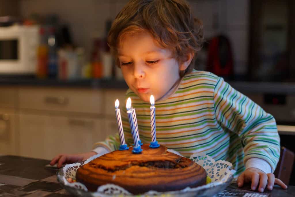Birthday party in the party room: child (age 4–6) blows out candles on cake at Chuck E. Cheese, pizza and games nearby.