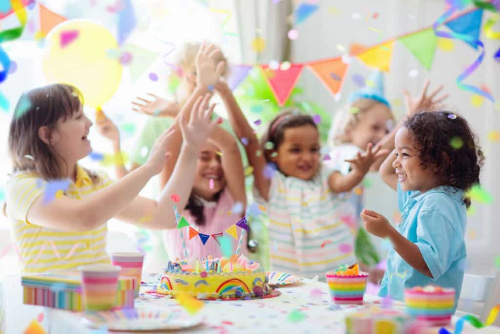 Birthday party in Chuck E. Cheese party room with smiling kids ages 5 to 8, balloons, pizza, decorated cake, and arcade games.