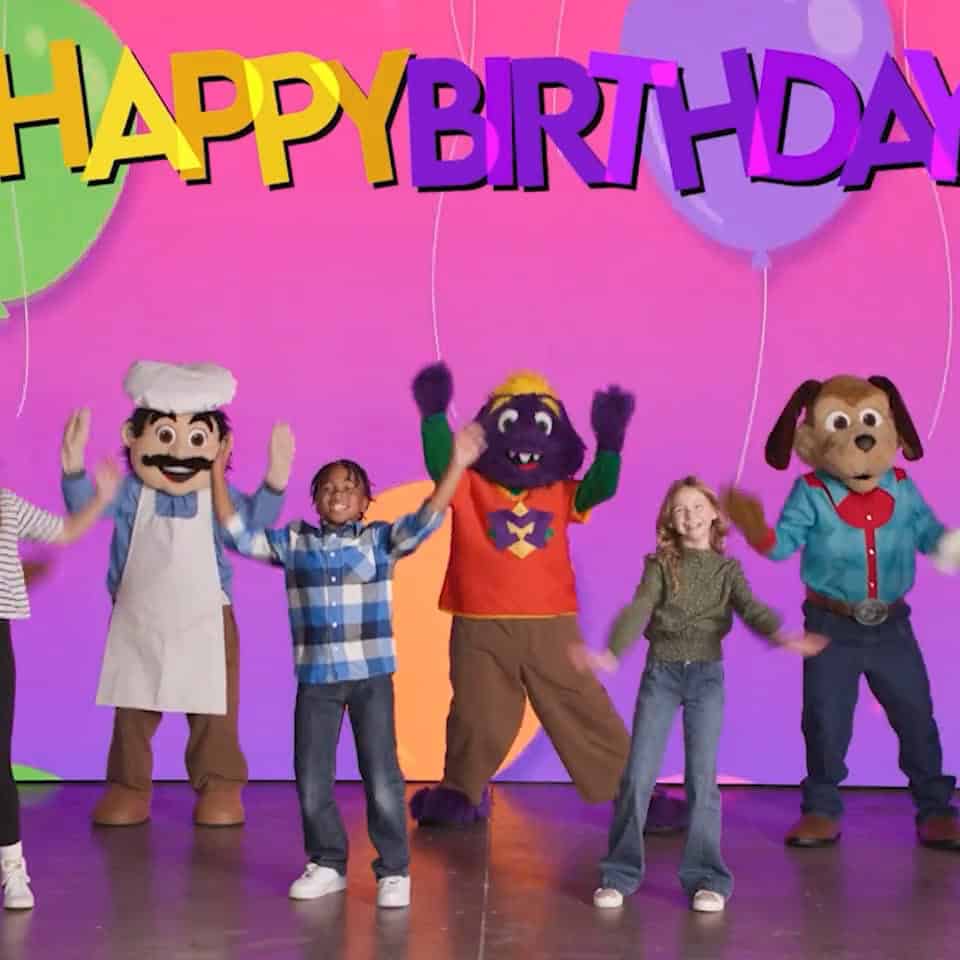 Kids and Chuck E. Cheese characters celebrate at a birthday party with balloons, a Happy Birthday sign, pizza, and arcade games.