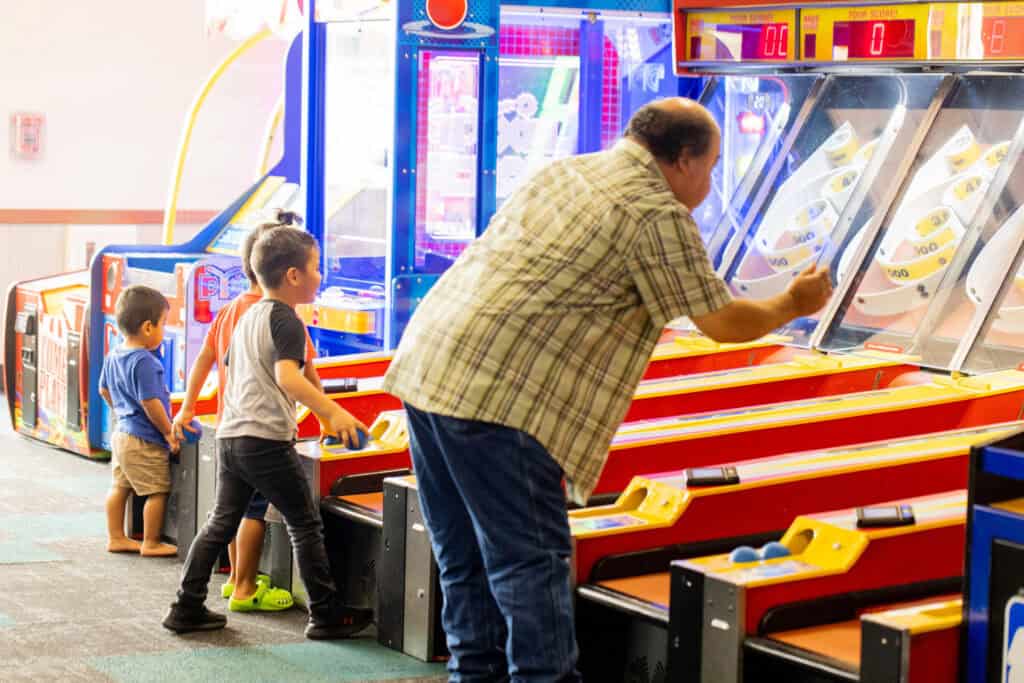 Grandfather and two young boys playing arcade games at Chuck E. Cheese.