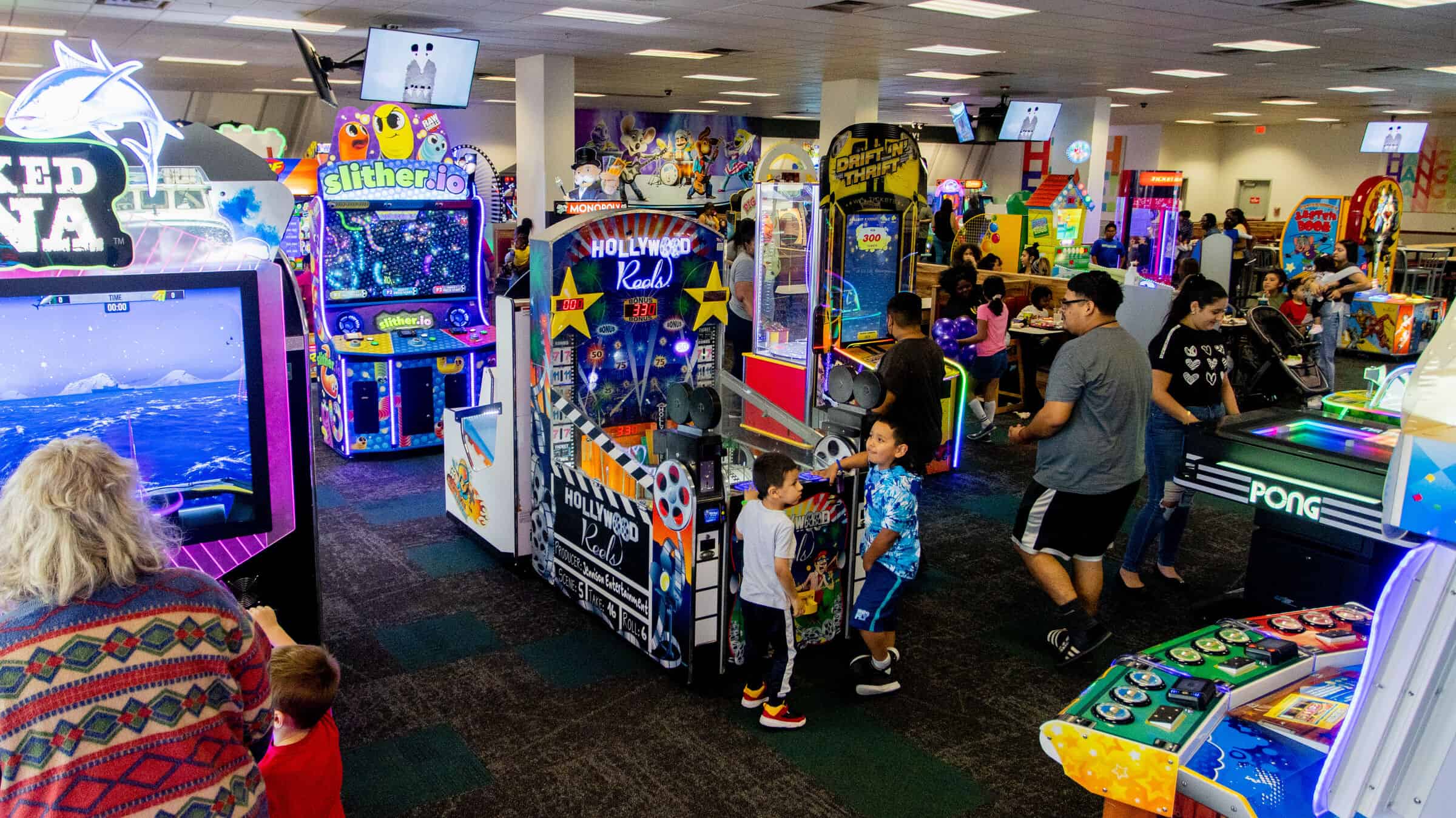 Kids playing arcade games at Chuck E. Cheese with bright colorful machines in the background.