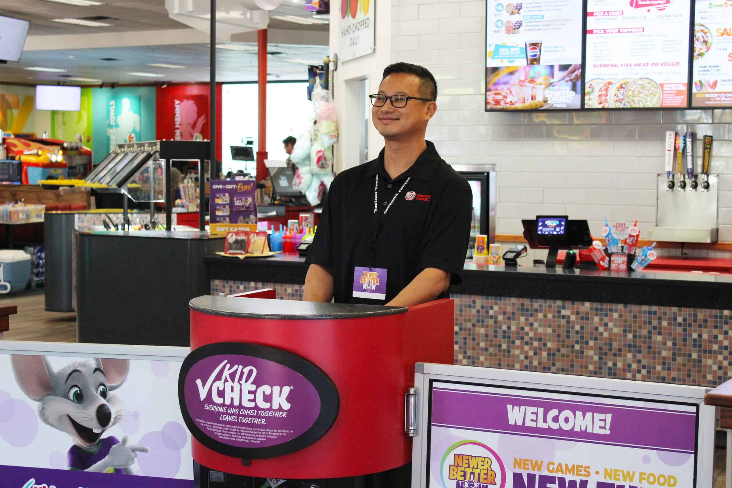 Chuck E. Cheese team member smiling at the Kid Check station, ensuring guest safety and welcome.