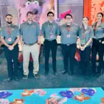 Chuck E. Cheese team, mostly young adults, stand in a party room with character posters and vibrant carpet at the family fun center.