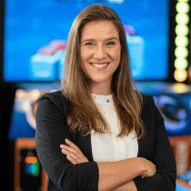 Woman with long brown hair smiles, arms crossed, in front of Chuck E. Cheese arcade games and kids birthday party setup.
