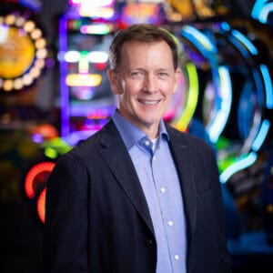 A man in a dark suit and light blue shirt smiles by arcade games for kids at Chuck E. Cheese, a family fun center for birthday parties.