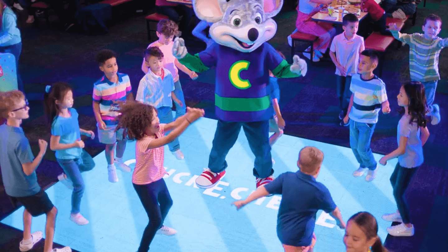 Children celebrate a birthday party dancing with Chuck E. Cheese in a family fun center with arcade games, pizza, and Fun Pass.