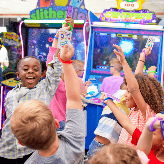 Kids celebrate with arms raised at a Chuck E. Cheese group event