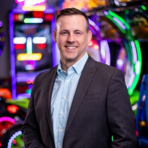 A man in a suit smiles near colorful arcade games at Chuck E. Cheese, a family fun center for kids entertainment and birthday parties.
