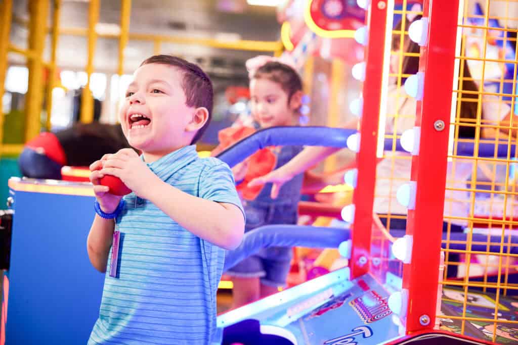Young boy, age 4-5, fully focused on playing an arcade game at Chuck E. Cheese, hands on controls, expression of pure concentration and delight