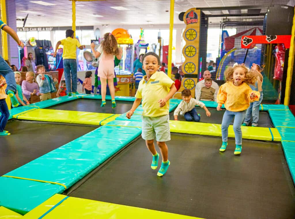 Kids celebrate a birthday party at Chuck E. Cheese, jumping, playing arcade games for kids, enjoying pizza and Fun Pass activities.
