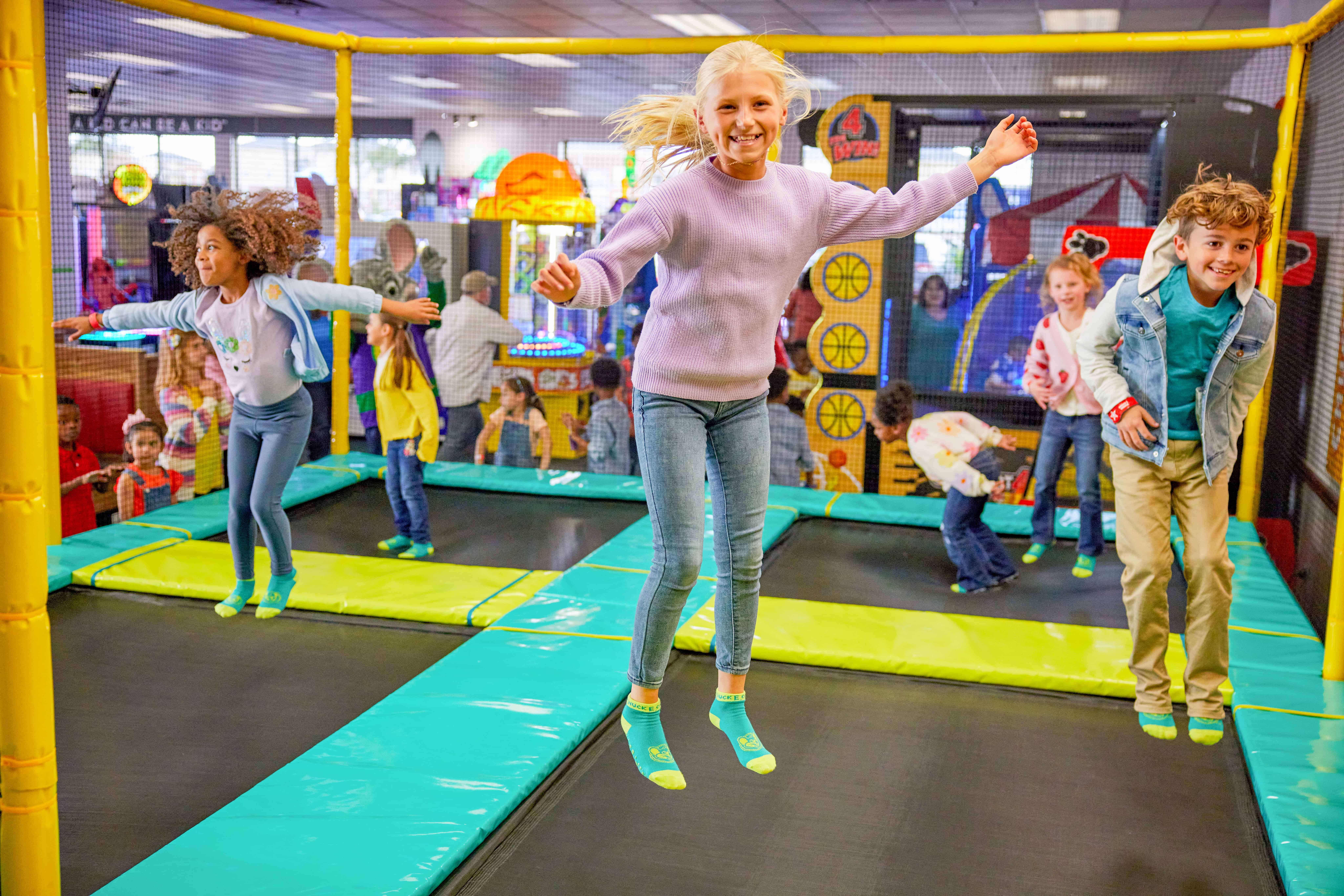 Young kids jumping on trampolines at Chuck E. Cheese in a bright, padded enclosure.