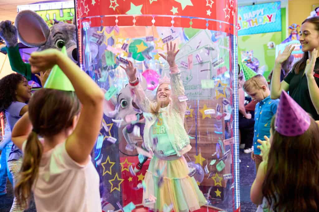 young girl inside chuck e. cheese ticket blaster at a chuck e cheese birthday party with chuck e cheese and friends