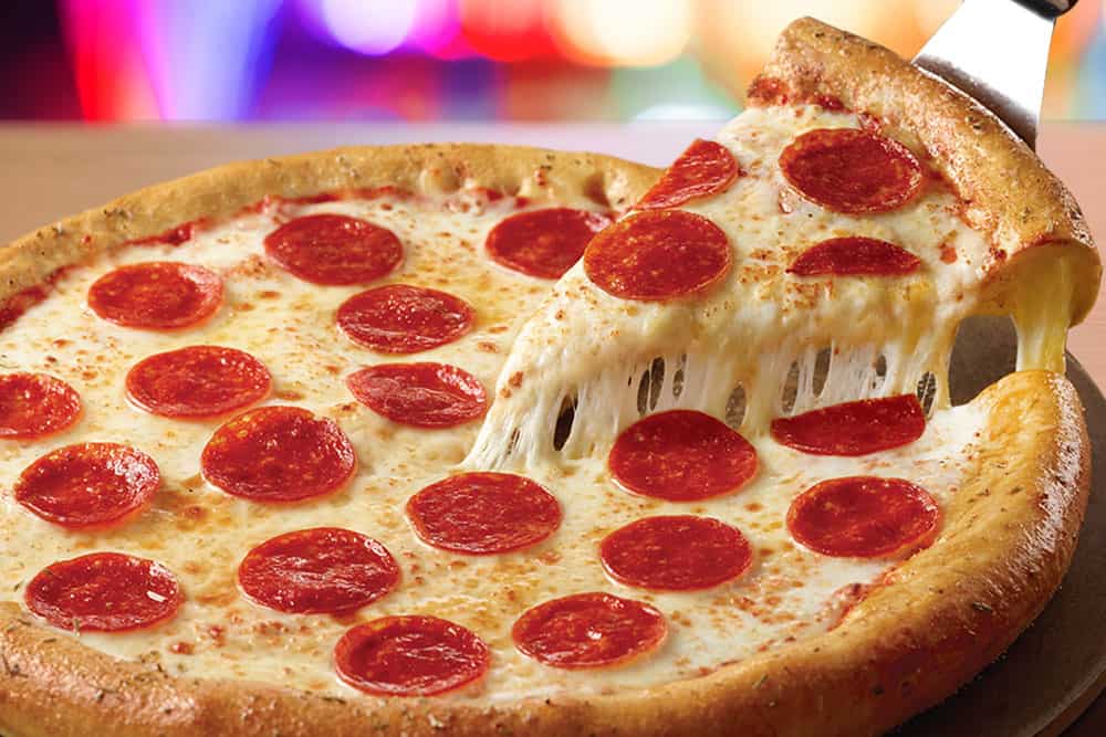 Pepperoni pizza slice being lifted, melted cheese stretching, at Chuck E. Cheese family fun center with arcade games for kids.