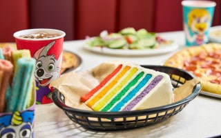 Rainbow layer cake, churros, salad, pizza, and kids' drink on a Chuck E. Cheese party table