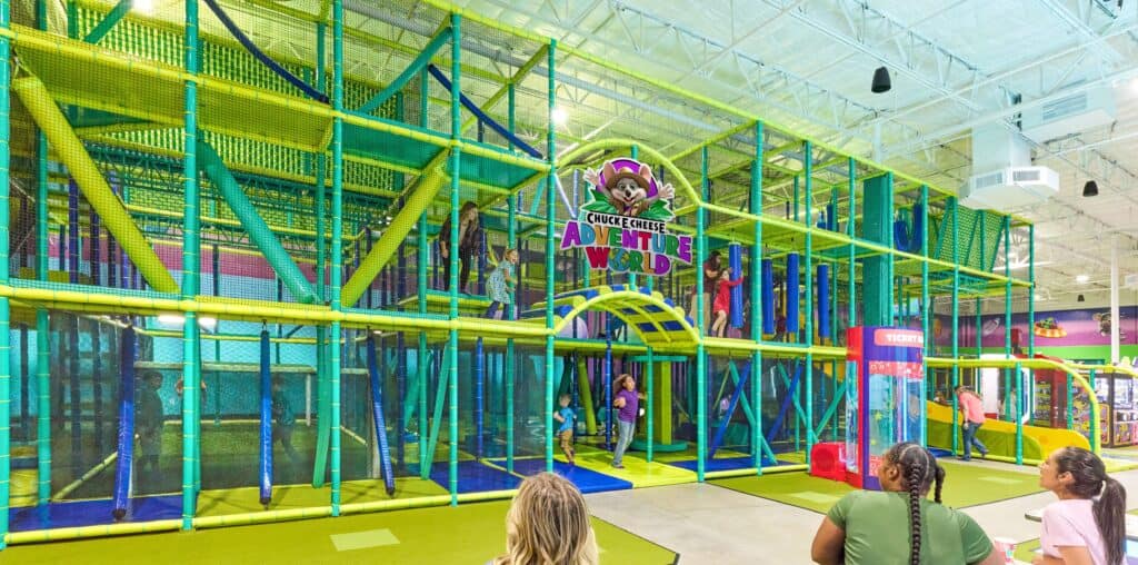 Kids enjoy indoor playground with yellow and green slides at Chuck E. Cheese; arcade games and pizza nearby for birthday parties.