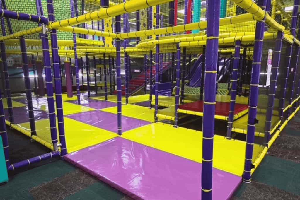 Chuck E. Cheese play area with purple and yellow padded floors, climbing structures, arcade games, and birthday party space.