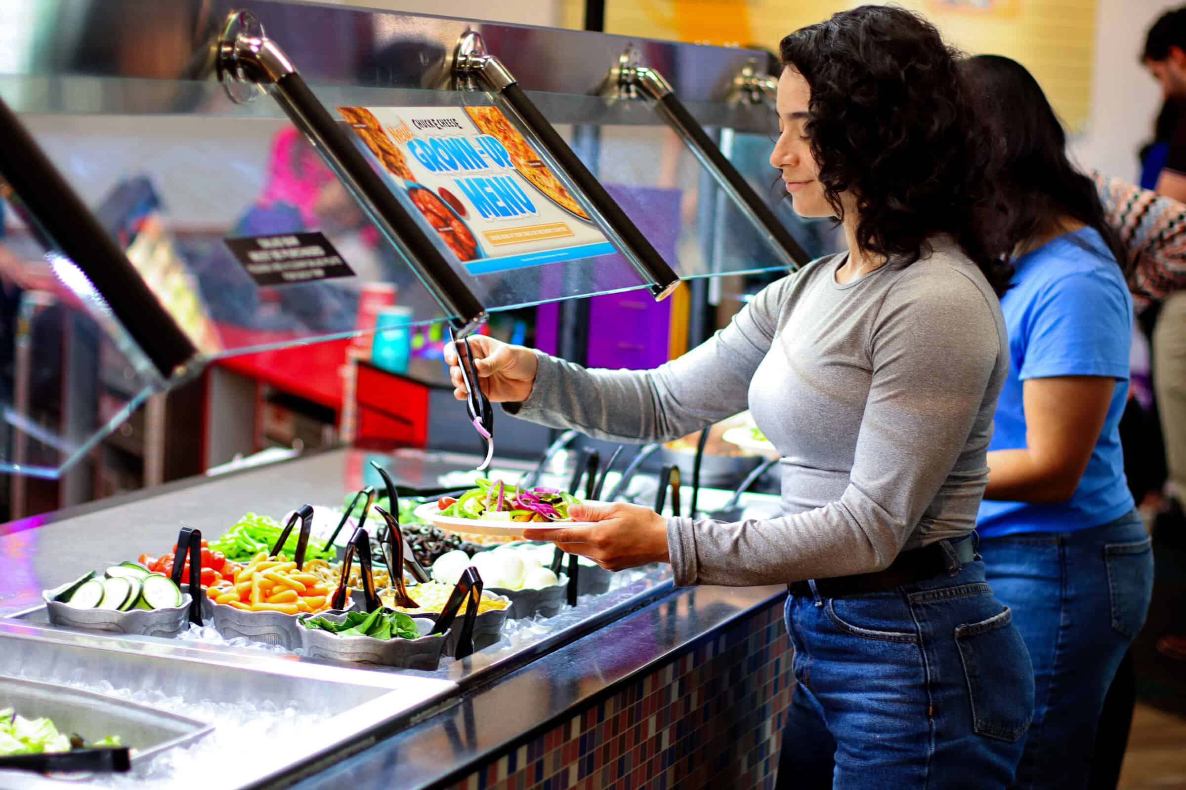 A woman gets salad at the Chuck E. Cheese buffet; other families enjoy their meals in the bright restaurant.