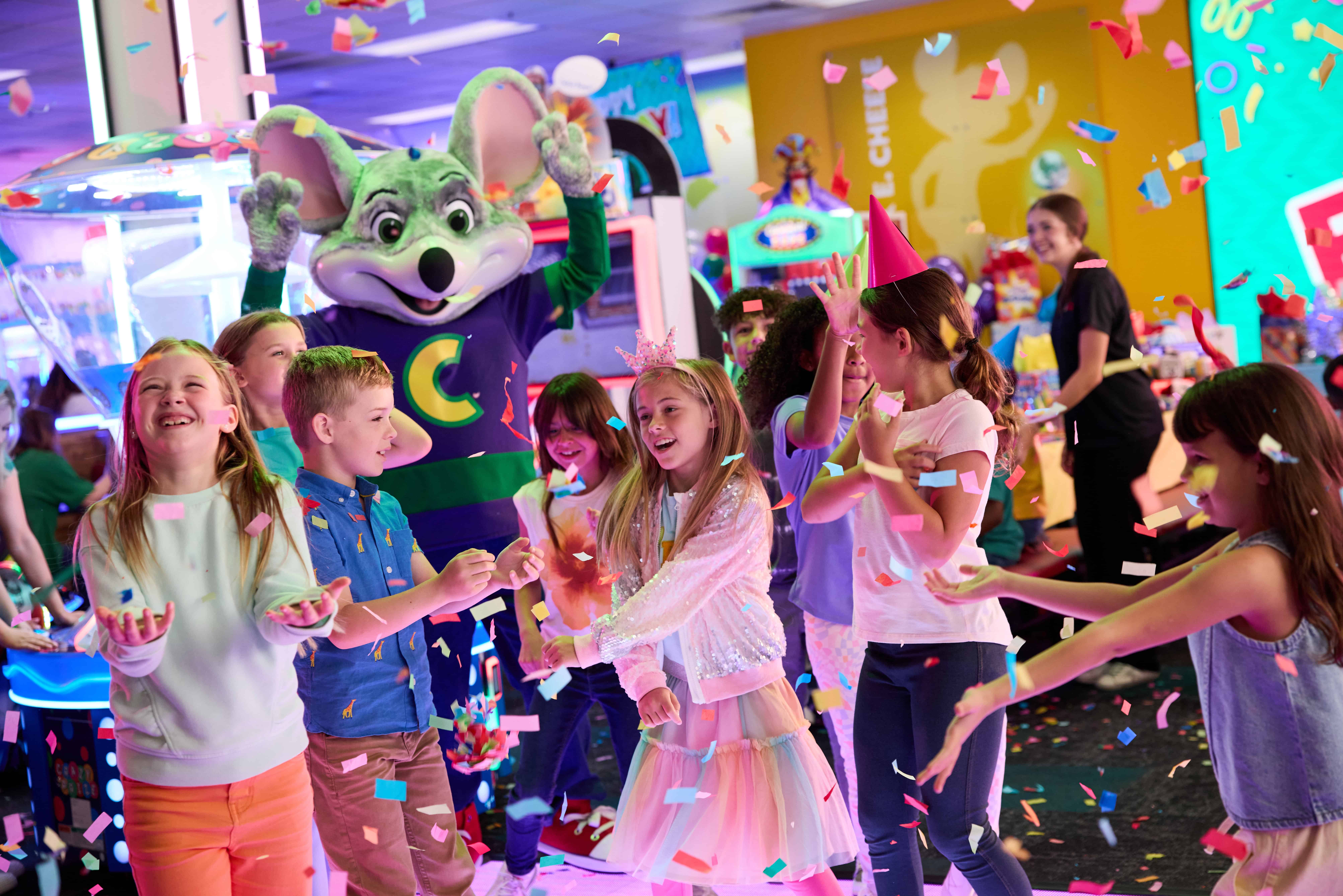 Kids dancing and celebrating at a Chuck E. Cheese birthday party with colorful decorations and arcade games.