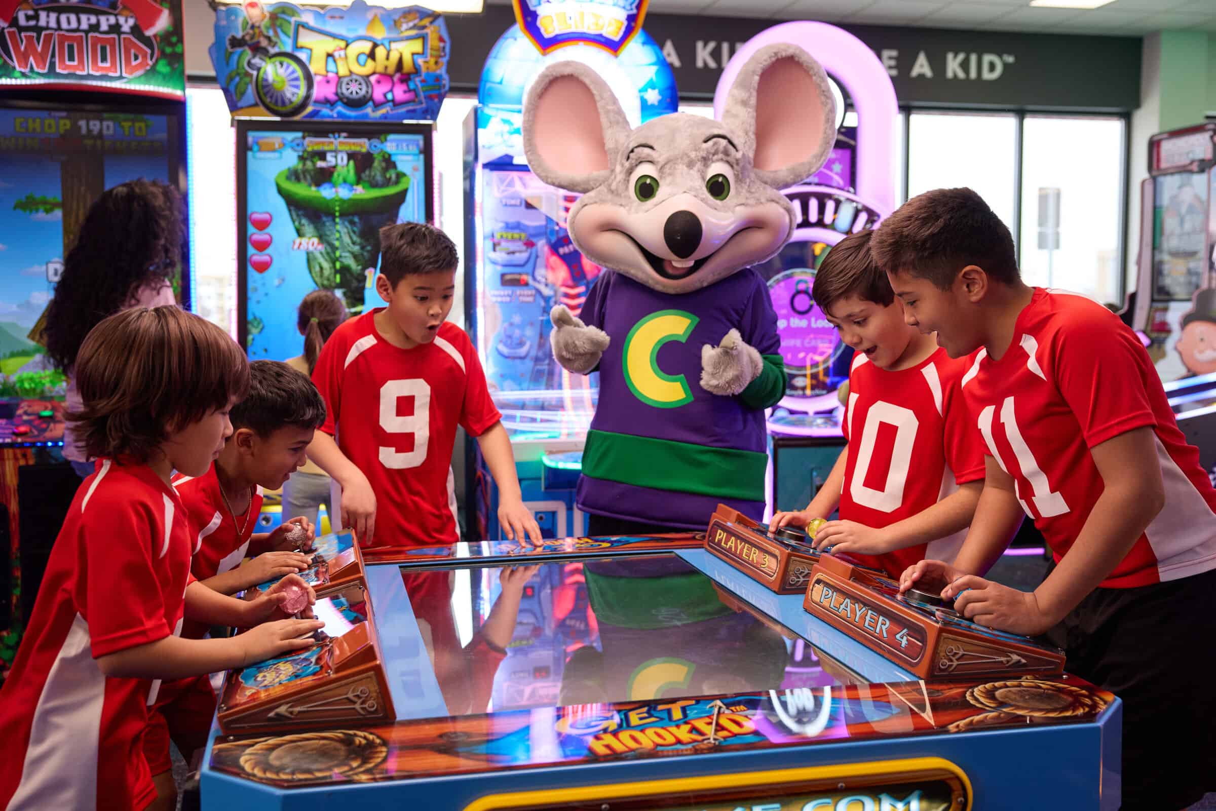 Kids in red soccer uniforms at an arcade machine at Chuck E. Cheese, playing games during their team event