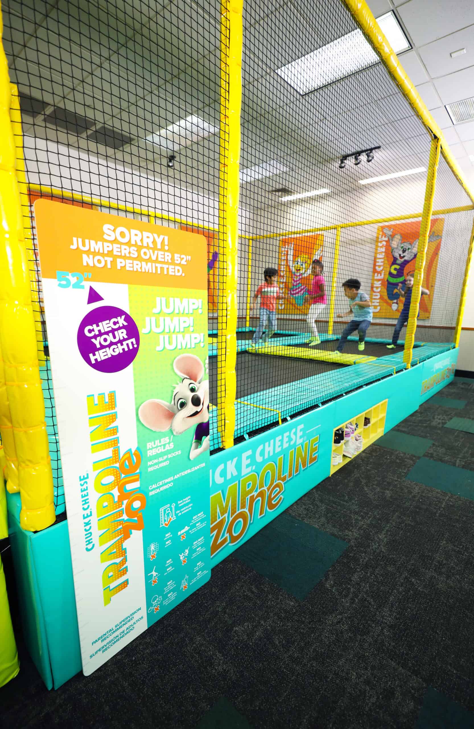 Kids jump in a netted Trampoline Zone at Chuck&nbsp;E.&nbsp;Cheese, with height rules posted and branding visible nearby.