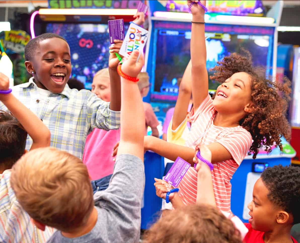 Kids at Chuck E. Cheese celebrate with tickets and prizes, showing off their winnings at a group event