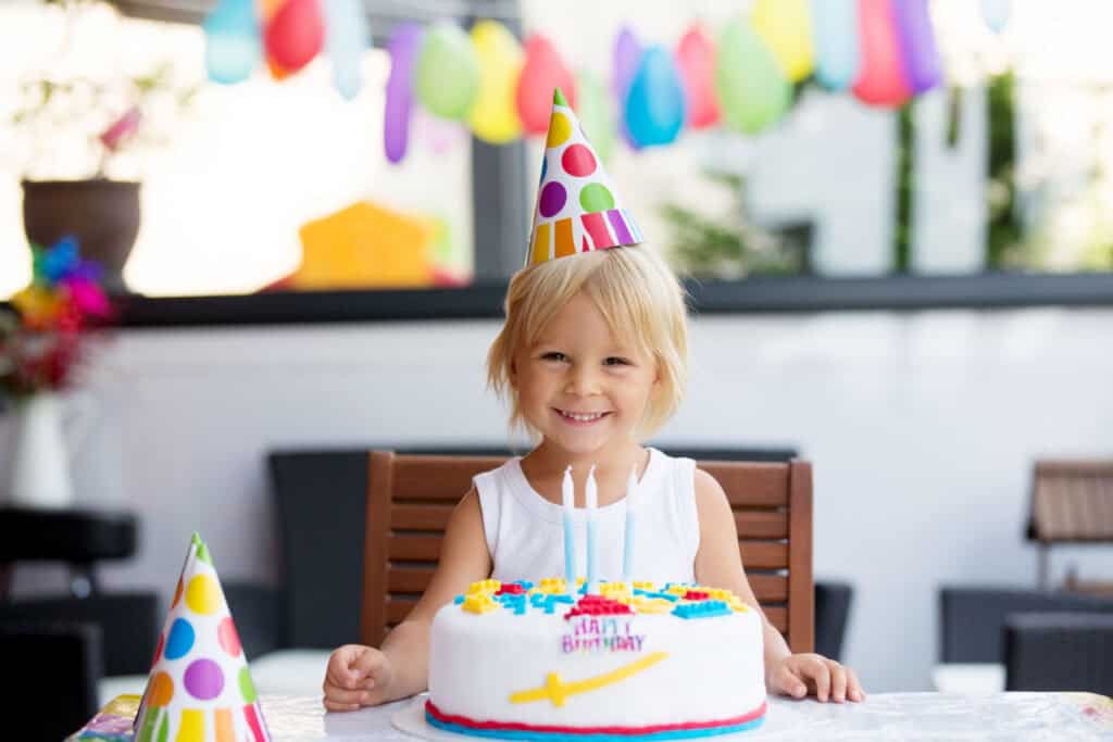 Young child celebrating their 4th birthday at a Chuck E. Cheese party room, surrounded by balloons, cake, and friends