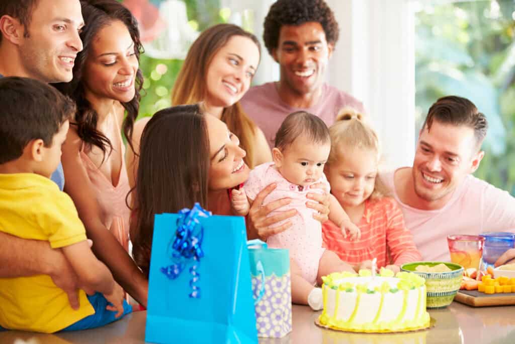 Party room birthday at Chuck&nbsp;E.&nbsp;Cheese: adults and kids, baby eyeing cake, gift bags on table, pizza and snacks ready for fun.