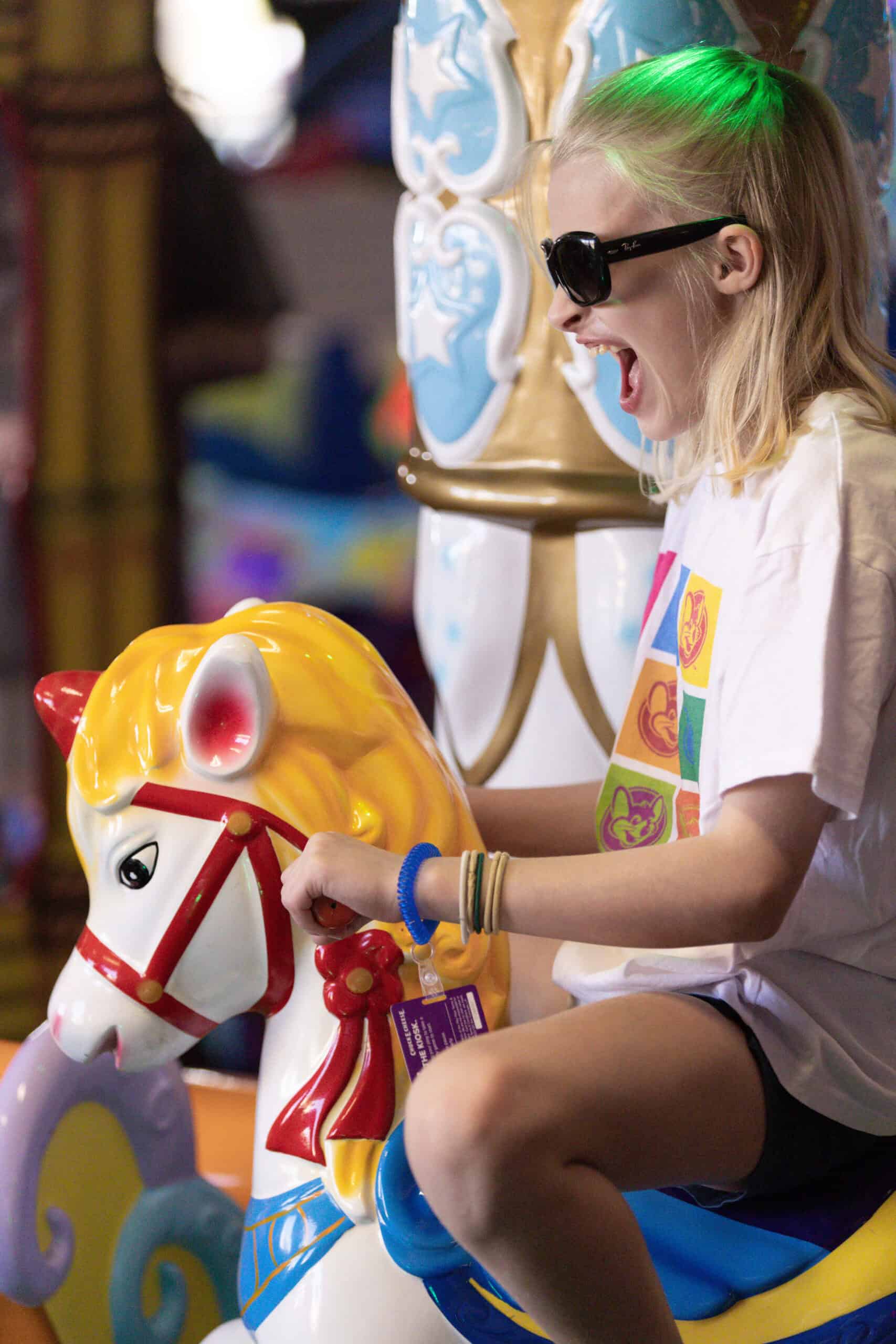 Excited girl wearing sunglasses and a Chuck E. Cheese shirt at a Sensory Sensitive Sunday event