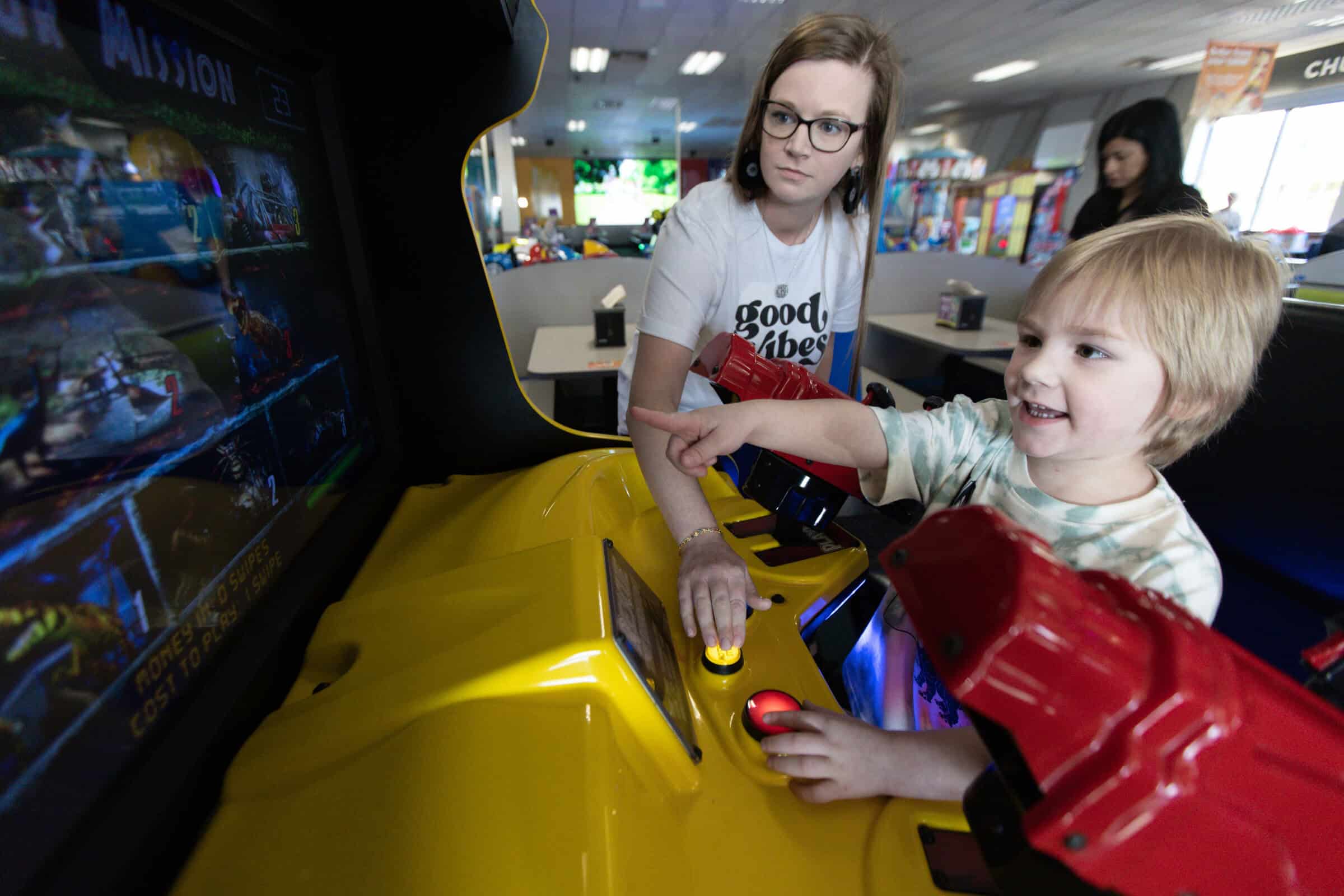 Mom and young child playing an arcade racing game together at Chuck E. Cheese