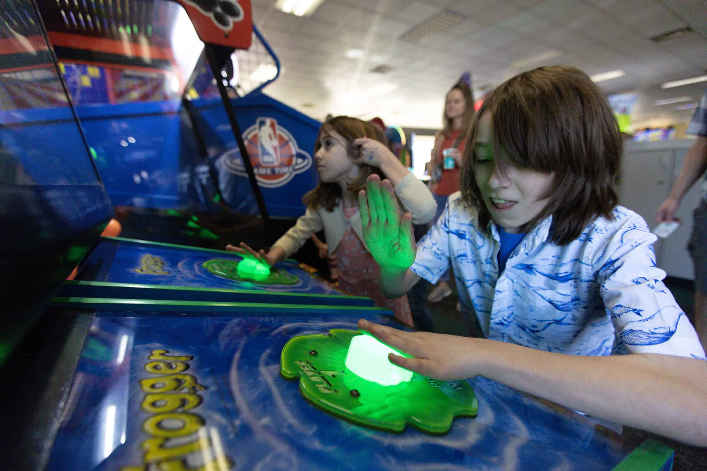 Kids playing a Frogger arcade game at Chuck E. Cheese, with one child fully focused on the controls